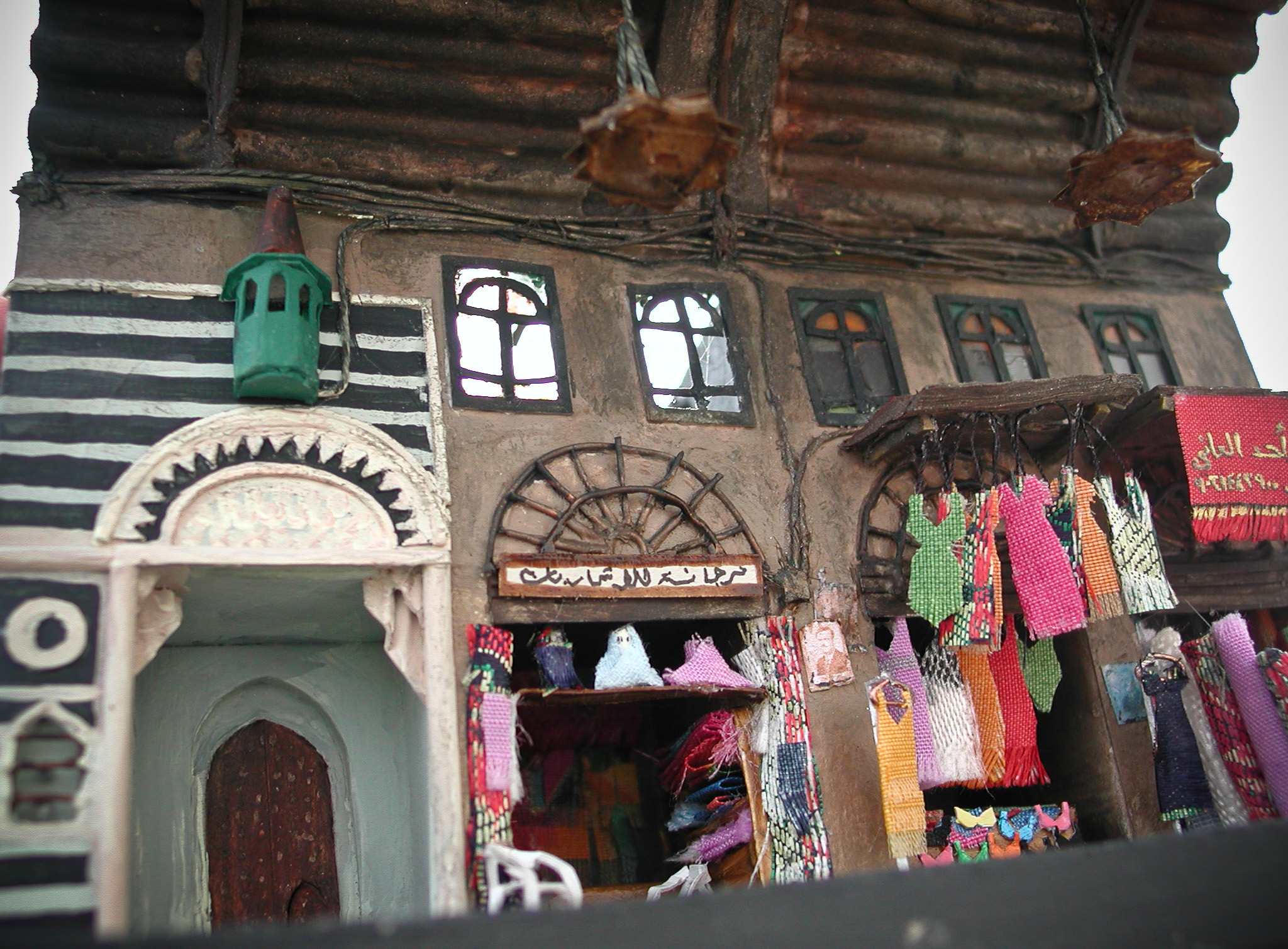 Vue sur l'entrée de la mosquée couverte et diverses boutiques de mode et tissus. Socle 13 x 7,5 cm.