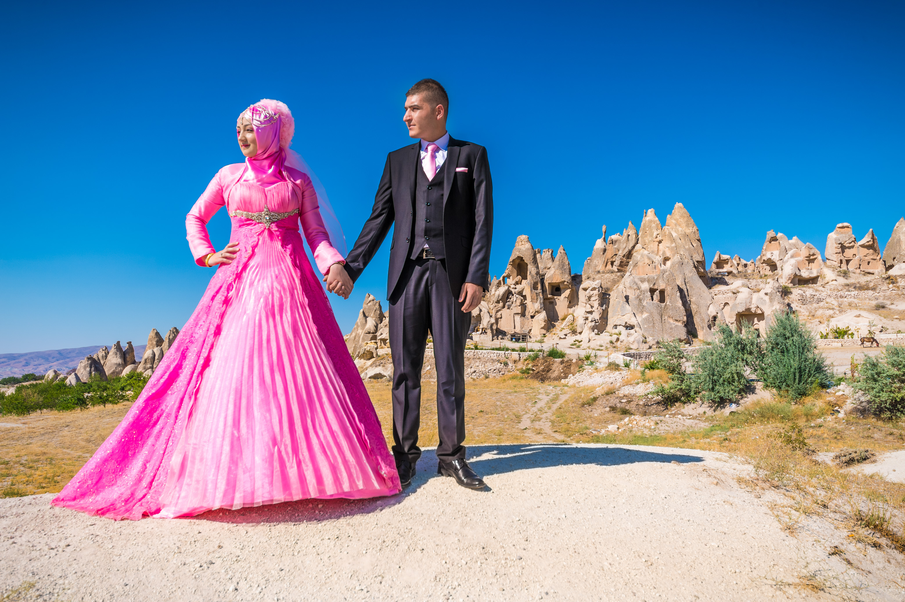 Turquie, Anatolie Centrale, province de Nevşehir, Cappadoce classée Patrimoine Mondial de l'UNESCO, Göreme, couple de jeunes mariés prenant la pose devant le paysage de collines de tuf volcanique, cheminées de fées et vestiges d'habitations troglodytiques dans le Parc National de Göreme // Turkey, Central Anatolia, Nevşehir province, Cappadocia UNESCO World Heritage Site, Göreme, newlywed couple posing in front of the landscape of volcanic tuff hills, fairy chimneys and vestiges of troglodyte dwellings in the Göreme National Park