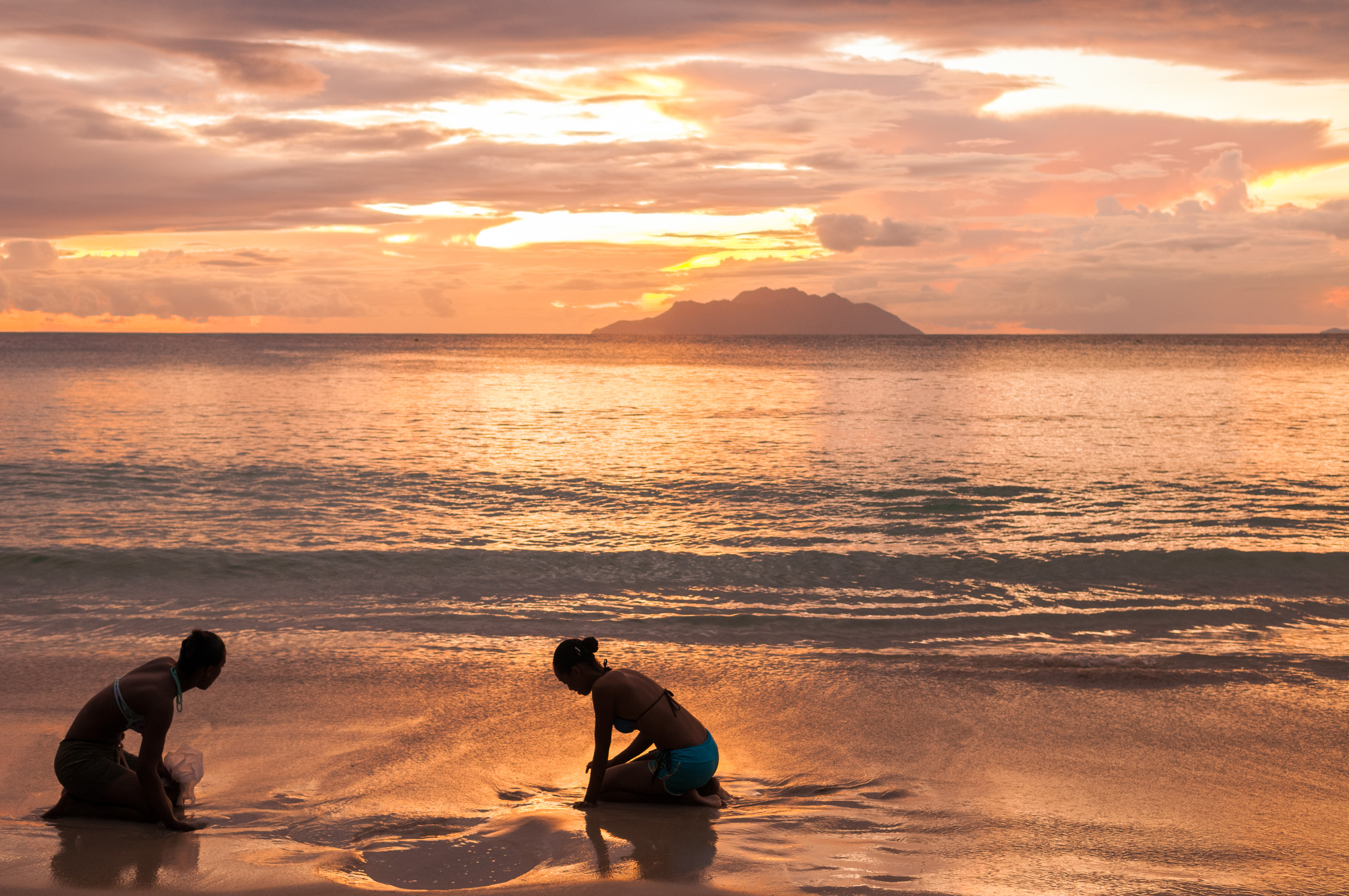 Seychelles, océan Indien, île de Mahé, Beau Vallon, jeunes femmes dessinant dans le sable au coucher de soleil, l'île de Silhouette en arrière-plan, plage de Beau Vallon // Seychelles, Indian Ocean, Mahe Island, Beau Vallon, young women drawing in the sand at sunset, Silhouette Island in the background, Beau Vallon beach