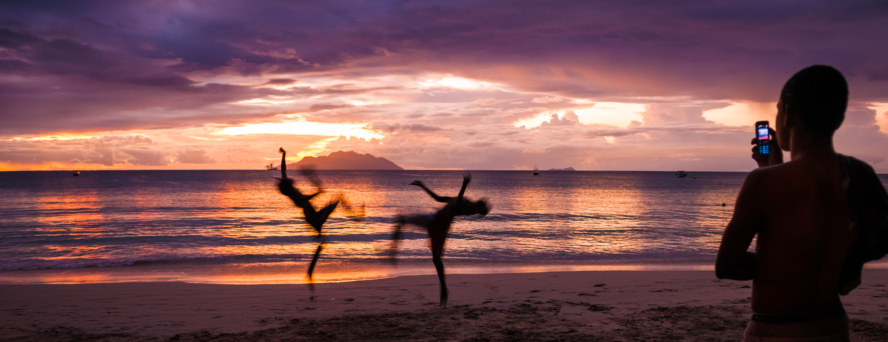 Seychelles, océan Indien, île de Mahé, Beau Vallon, jeunes hommes jouant à la capoeira au coucher de soleil, l'île de Silhouette en arrière-plan, plage de Beau Vallon en vue panoramique // Seychelles, Indian Ocean, Mahe Island, Beau Vallon, young men playing capoeira at sunset, Silhouette Island in the background, Beau Vallon beach panoramic view